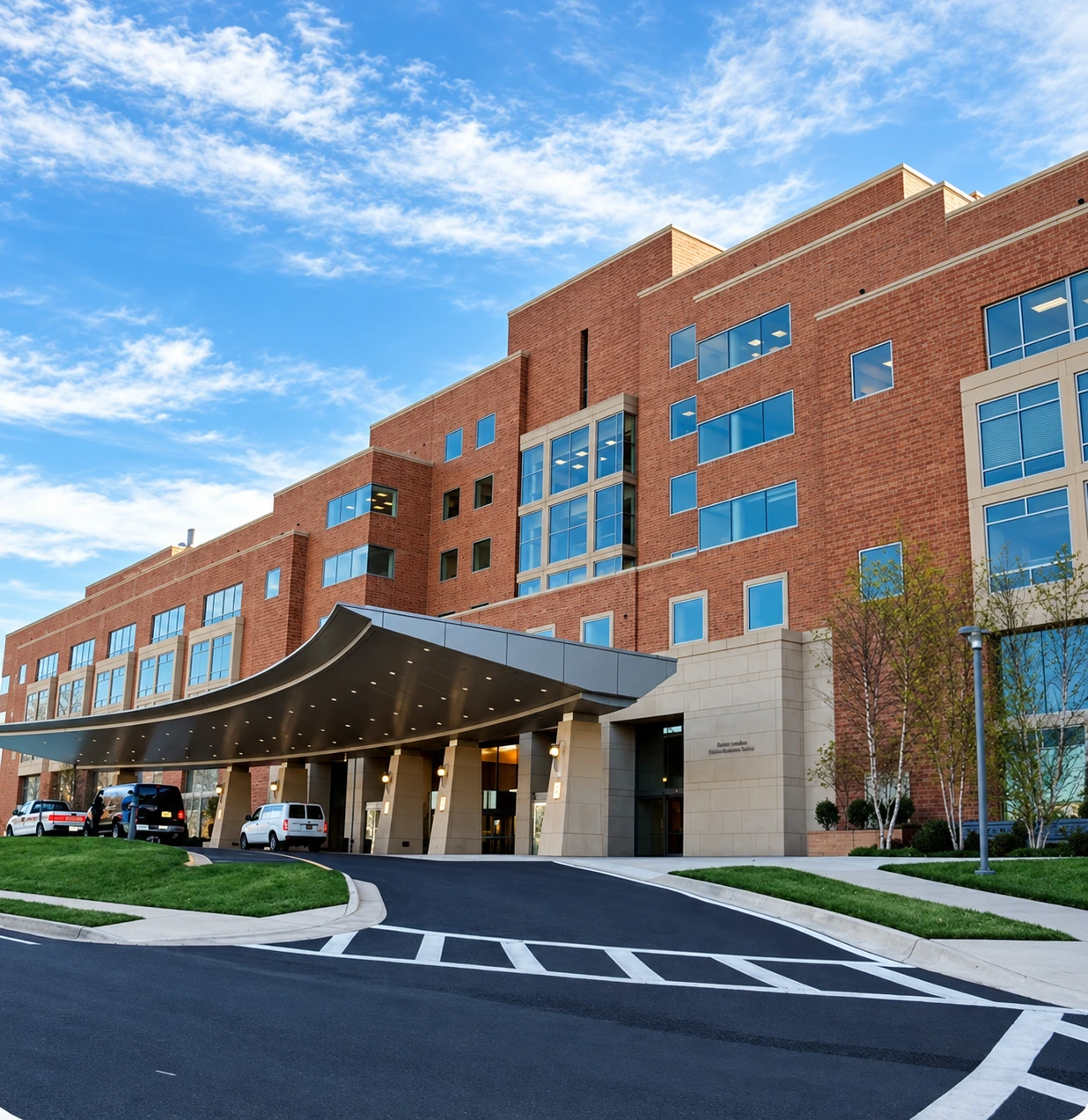 Modern brick hospital building with a curved entrance canopy under a blue sky, representing healthcare and clinical research partnerships